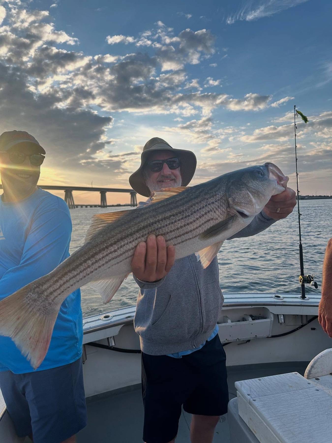 An angler holding a large striped bass aboard Anna Maria at sunset near Hampton Bays