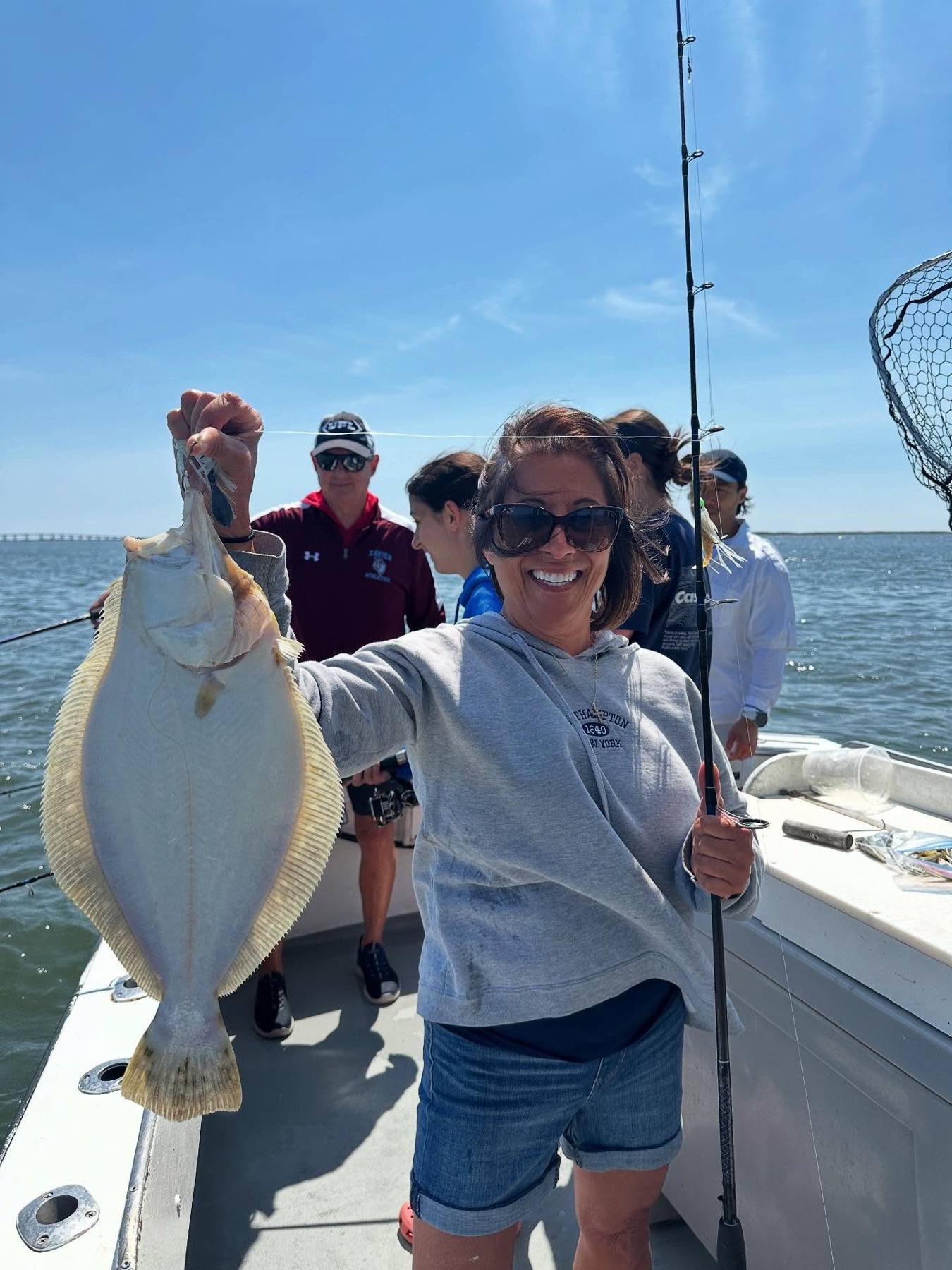 An adult angler smiling and holding a large fluke aboard the fishing boat